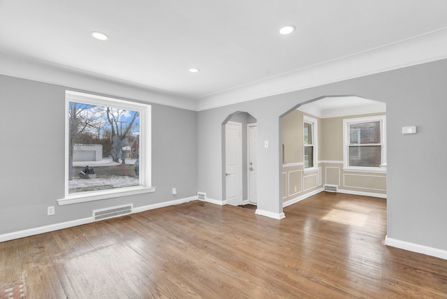 empty room featuring arched walkways, recessed lighting, wood finished floors, visible vents, and baseboards