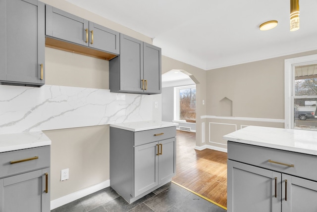 kitchen featuring dark wood-style floors, arched walkways, light stone counters, backsplash, and gray cabinetry