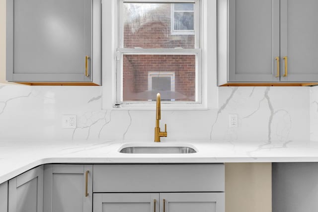 interior details featuring light stone counters, gray cabinets, a sink, and decorative backsplash