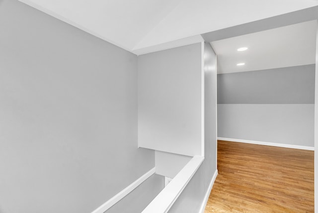 hallway featuring lofted ceiling, baseboards, wood finished floors, and recessed lighting