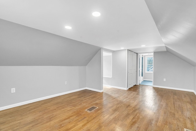 additional living space with baseboards, vaulted ceiling, visible vents, and light wood-style floors