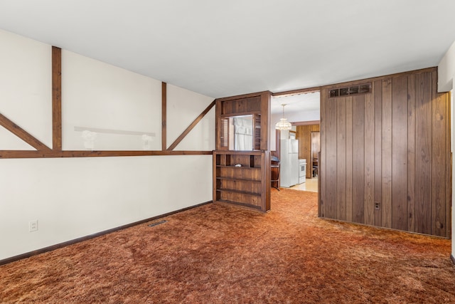 empty room with carpet floors, wood walls, visible vents, and baseboards