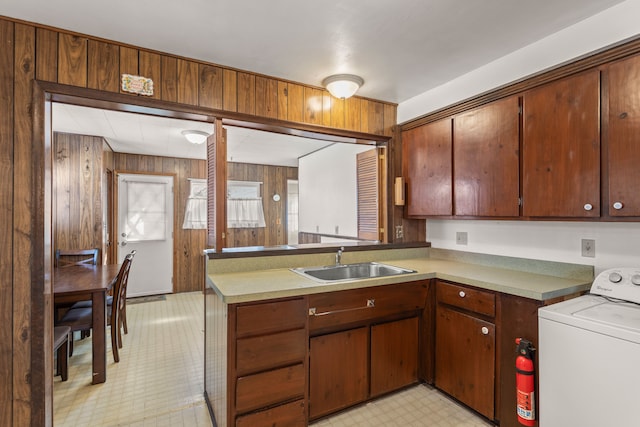 kitchen with wooden walls, washer / clothes dryer, a peninsula, light floors, and a sink