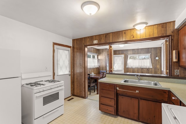 kitchen featuring white appliances, a sink, wood walls, and light floors