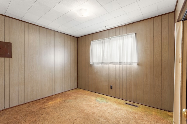 spare room featuring wood walls, carpet, and visible vents