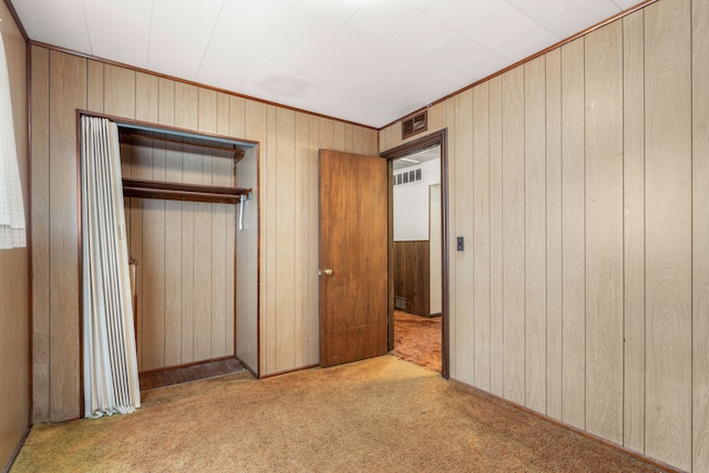 unfurnished bedroom featuring a closet, carpet, visible vents, and wooden walls