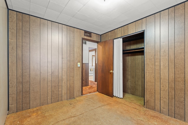 unfurnished bedroom with carpet floors, wood walls, a closet, and visible vents