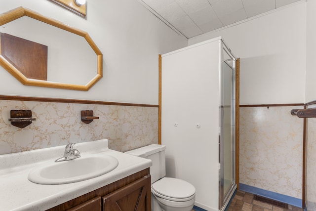 bathroom featuring toilet, wainscoting, vanity, a shower stall, and wallpapered walls