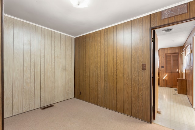 carpeted spare room with wooden walls, visible vents, and crown molding