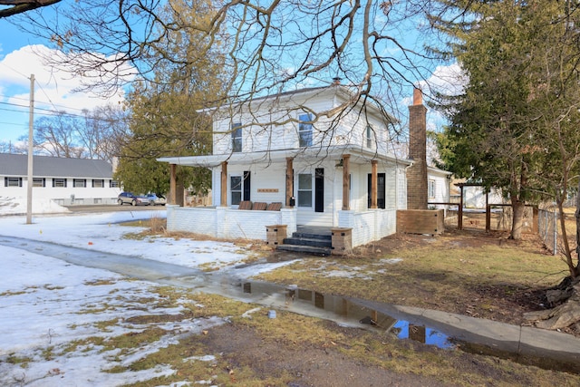 view of front of house with a porch, a chimney, and fence