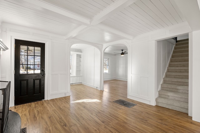 foyer featuring arched walkways, wood finished floors, stairs, a decorative wall, and beam ceiling