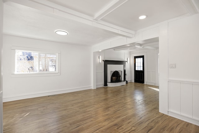 unfurnished living room with a brick fireplace, a decorative wall, beamed ceiling, and wood finished floors