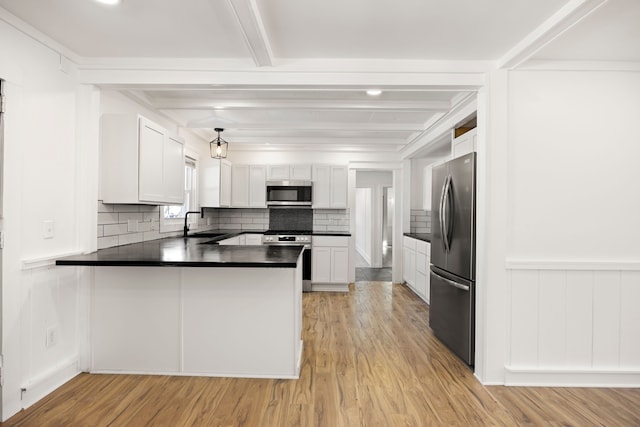 kitchen with dark countertops, appliances with stainless steel finishes, beamed ceiling, a peninsula, and light wood-type flooring