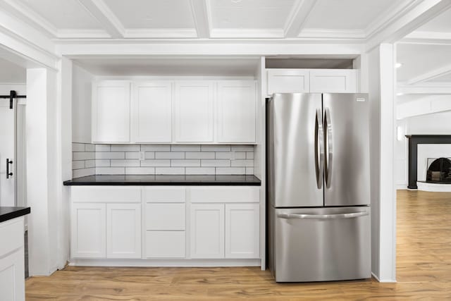 kitchen with light wood finished floors, a barn door, white cabinets, dark countertops, and freestanding refrigerator