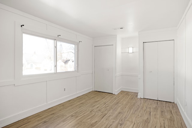 unfurnished bedroom with light wood-style flooring, visible vents, and a decorative wall