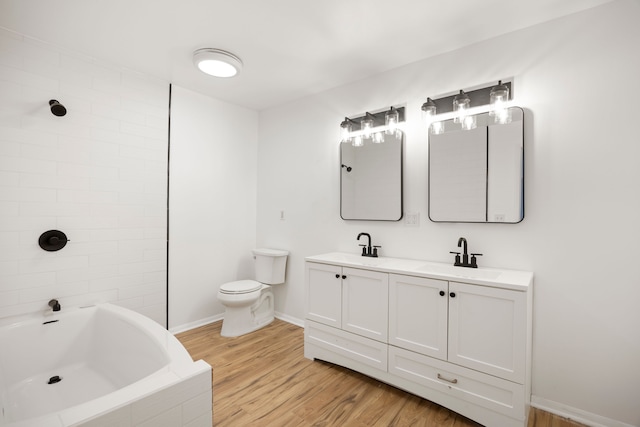 full bathroom featuring toilet, wood finished floors, a sink, baseboards, and double vanity