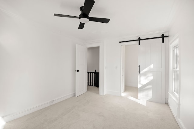 unfurnished bedroom with carpet floors, a barn door, ornamental molding, ceiling fan, and baseboards