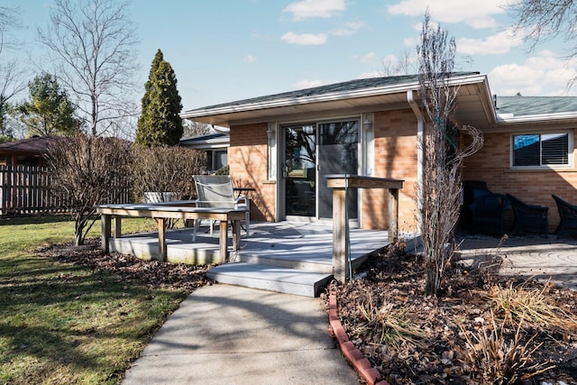 view of front of property with brick siding, fence, a deck, and a front lawn