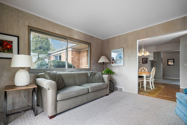 carpeted living area featuring a notable chandelier, visible vents, and crown molding