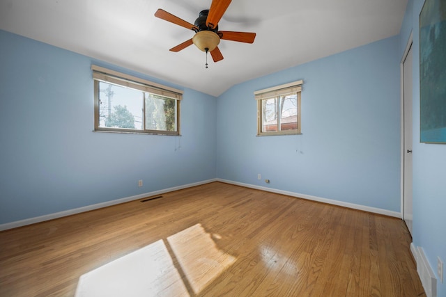 empty room with visible vents, a ceiling fan, vaulted ceiling, wood finished floors, and baseboards