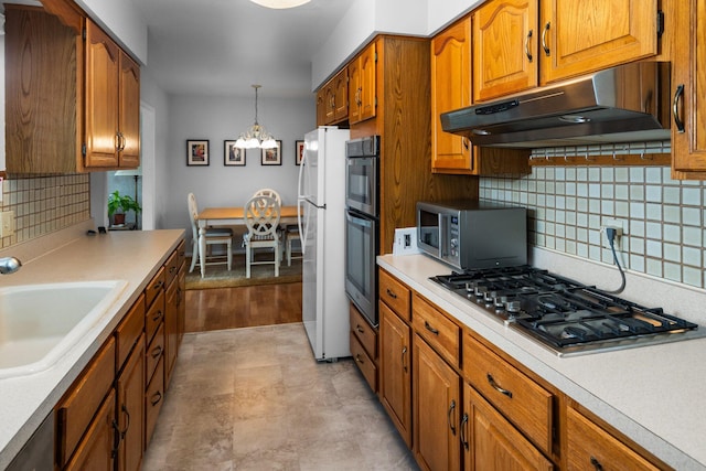 kitchen with brown cabinetry, appliances with stainless steel finishes, light countertops, under cabinet range hood, and a sink