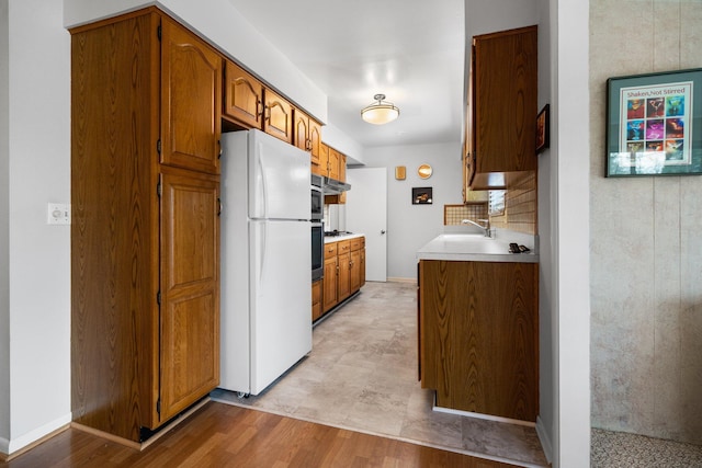 kitchen featuring light wood-style flooring, brown cabinets, freestanding refrigerator, light countertops, and a sink