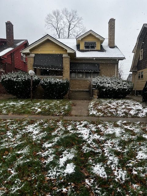 snow covered back of property featuring brick siding and a chimney