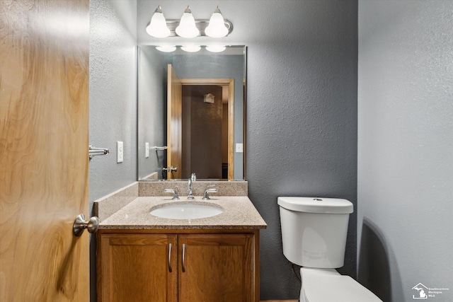 bathroom with a textured wall, vanity, and toilet