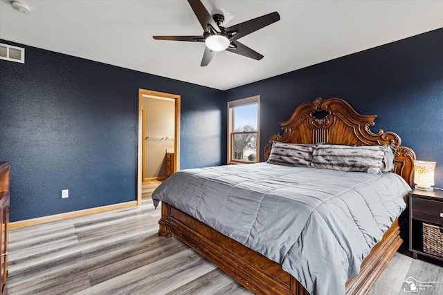 bedroom featuring ceiling fan, wood finished floors, visible vents, baseboards, and ensuite bath