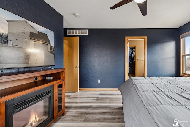 bedroom with a large fireplace, visible vents, a textured wall, and wood finished floors