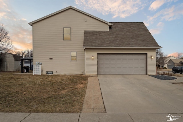 traditional-style home with an attached garage, a shingled roof, concrete driveway, and a yard