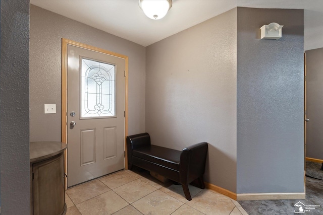 foyer entrance with light tile patterned flooring, a textured wall, and baseboards