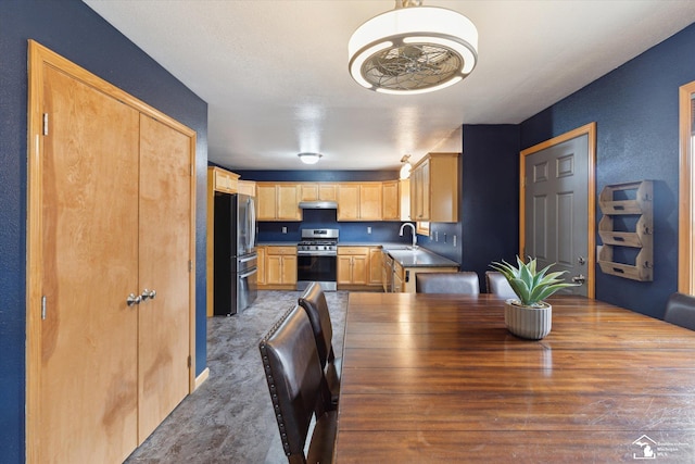 kitchen with light brown cabinetry, appliances with stainless steel finishes, carpet flooring, a sink, and under cabinet range hood