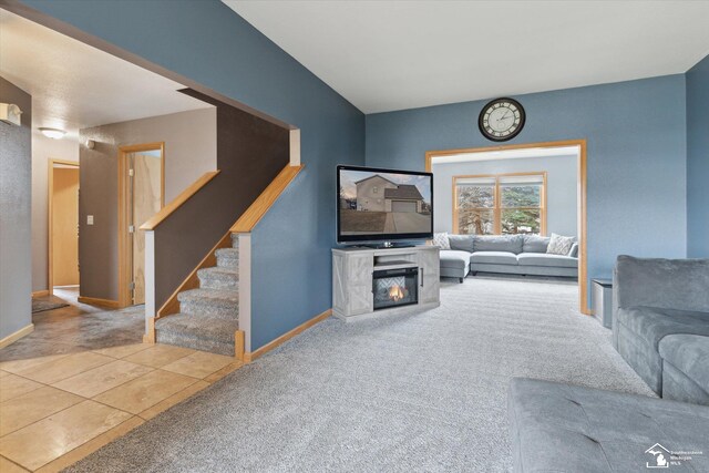 carpeted living room with a glass covered fireplace, tile patterned flooring, stairway, and baseboards