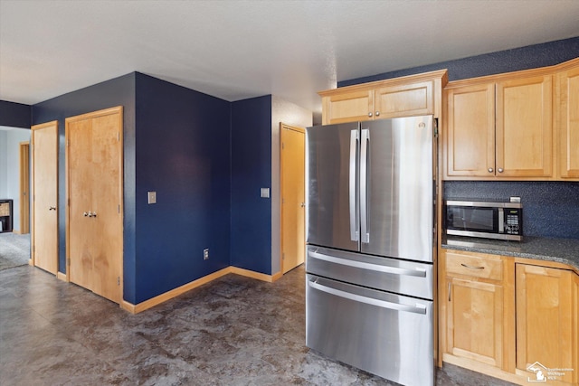 kitchen featuring stainless steel appliances, light brown cabinetry, dark countertops, and baseboards