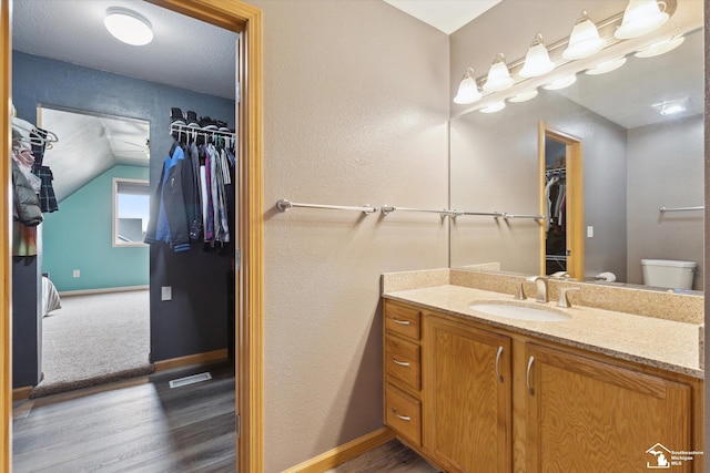 bathroom with baseboards, toilet, wood finished floors, vaulted ceiling, and vanity