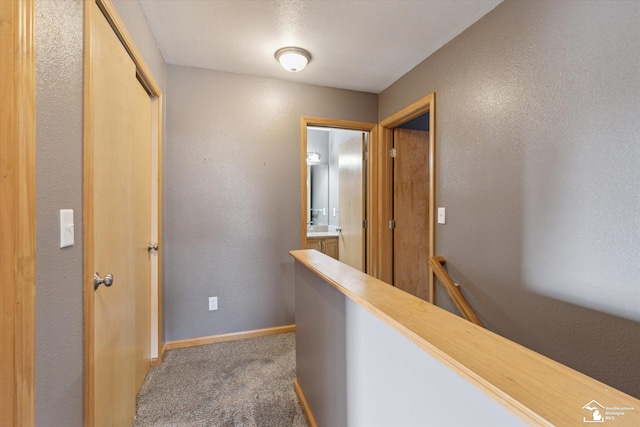 corridor featuring carpet, baseboards, a textured wall, and an upstairs landing