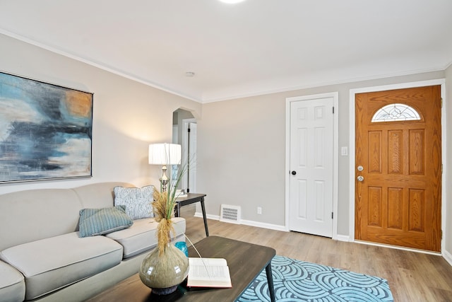 living room with visible vents, baseboards, ornamental molding, light wood-style flooring, and arched walkways