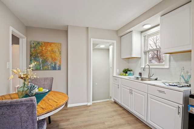 kitchen with light wood finished floors, a sink, decorative backsplash, light countertops, and white cabinetry