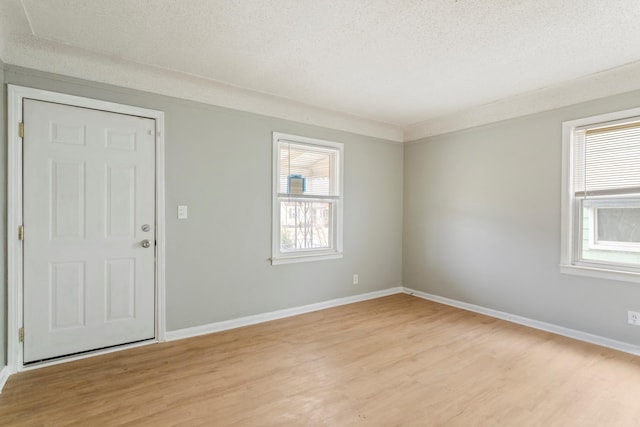 spare room featuring a healthy amount of sunlight, light wood-style flooring, baseboards, and a textured ceiling