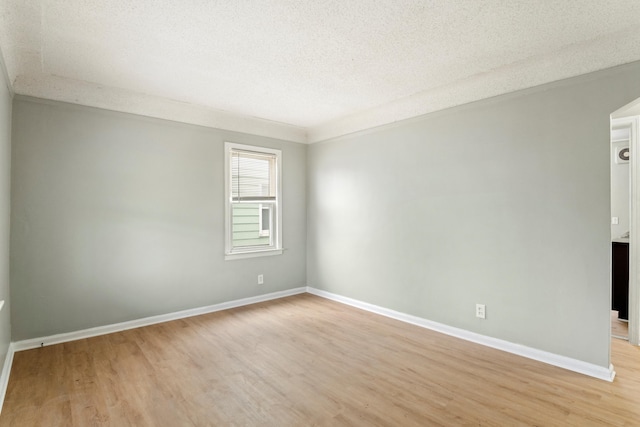 empty room with light wood-style flooring, baseboards, and a textured ceiling