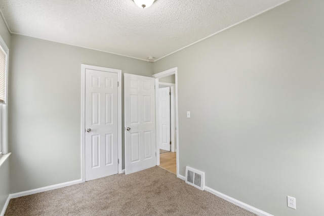 unfurnished bedroom with a textured ceiling, carpet flooring, visible vents, and baseboards