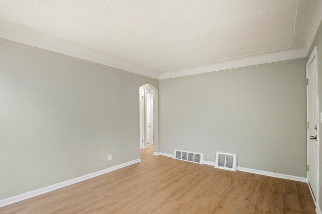 spare room with light wood-type flooring, baseboards, visible vents, and arched walkways