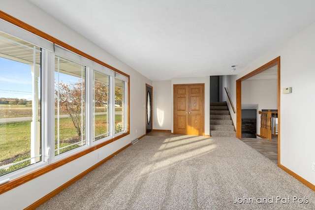 empty room with carpet floors, stairway, a wealth of natural light, and baseboards