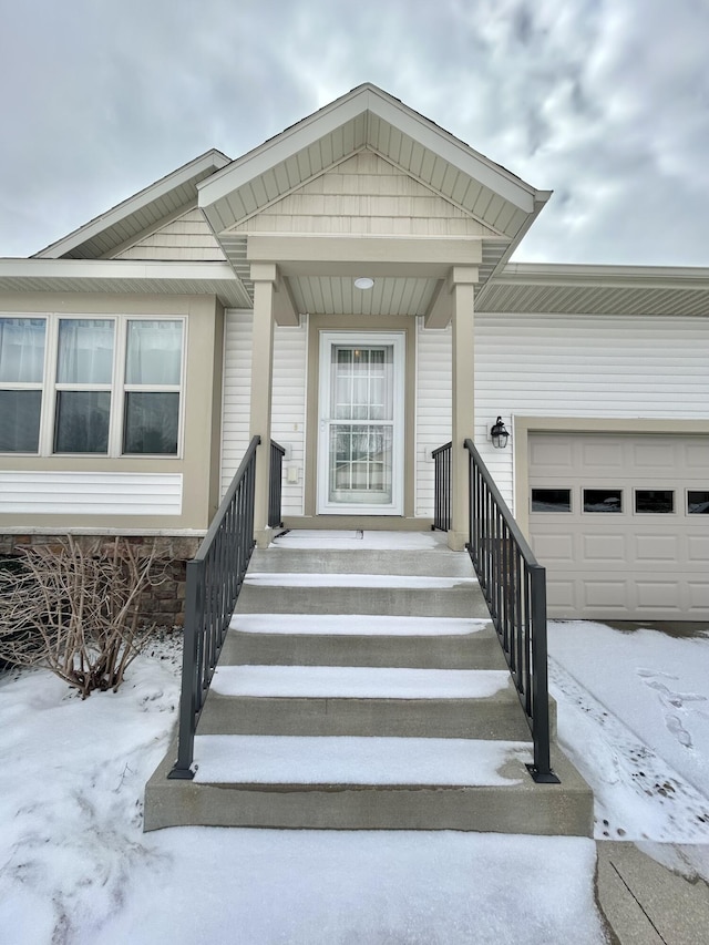 snow covered property entrance featuring an attached garage