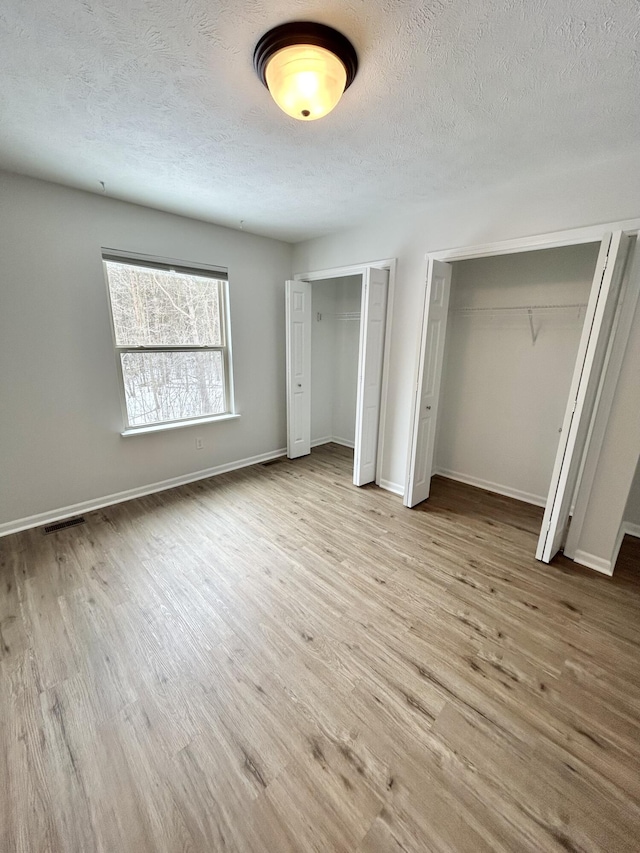 unfurnished bedroom featuring baseboards, visible vents, wood finished floors, a textured ceiling, and two closets