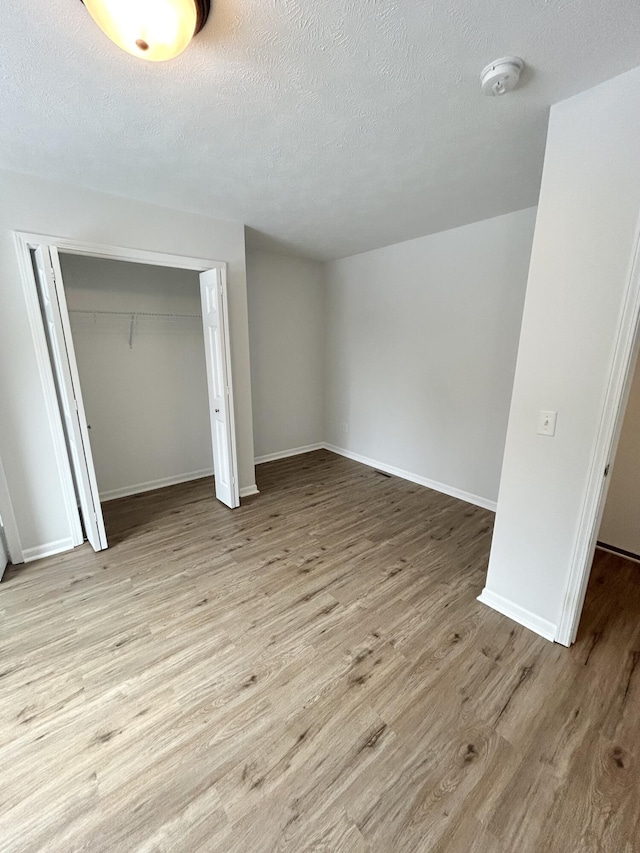 unfurnished bedroom featuring a closet, a textured ceiling, baseboards, and wood finished floors