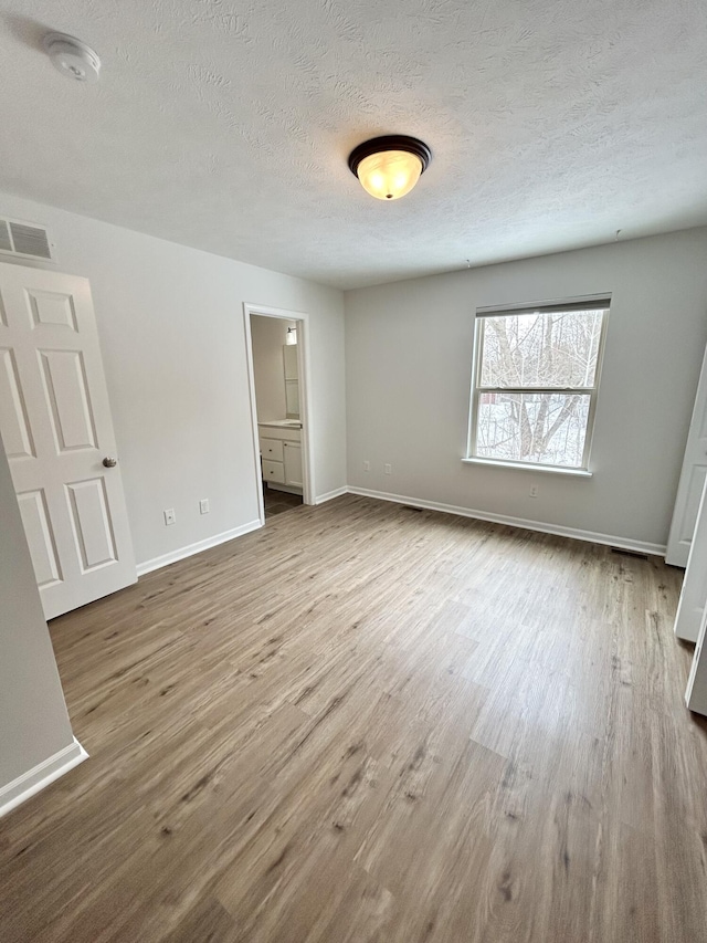 unfurnished bedroom with a textured ceiling, wood finished floors, visible vents, and baseboards