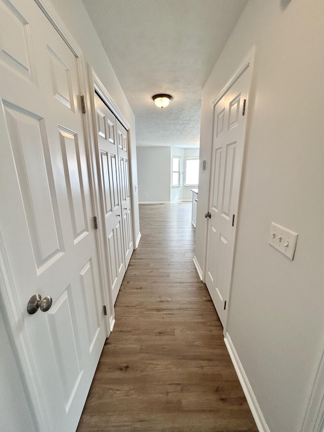 hall with dark wood-style floors, baseboards, and a textured ceiling