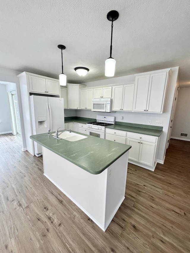 kitchen featuring dark countertops, white cabinetry, a sink, wood finished floors, and white appliances